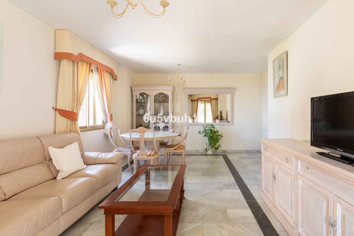 A spacious living and dining room with a beige sofa, dining table, cabinet, and television set.