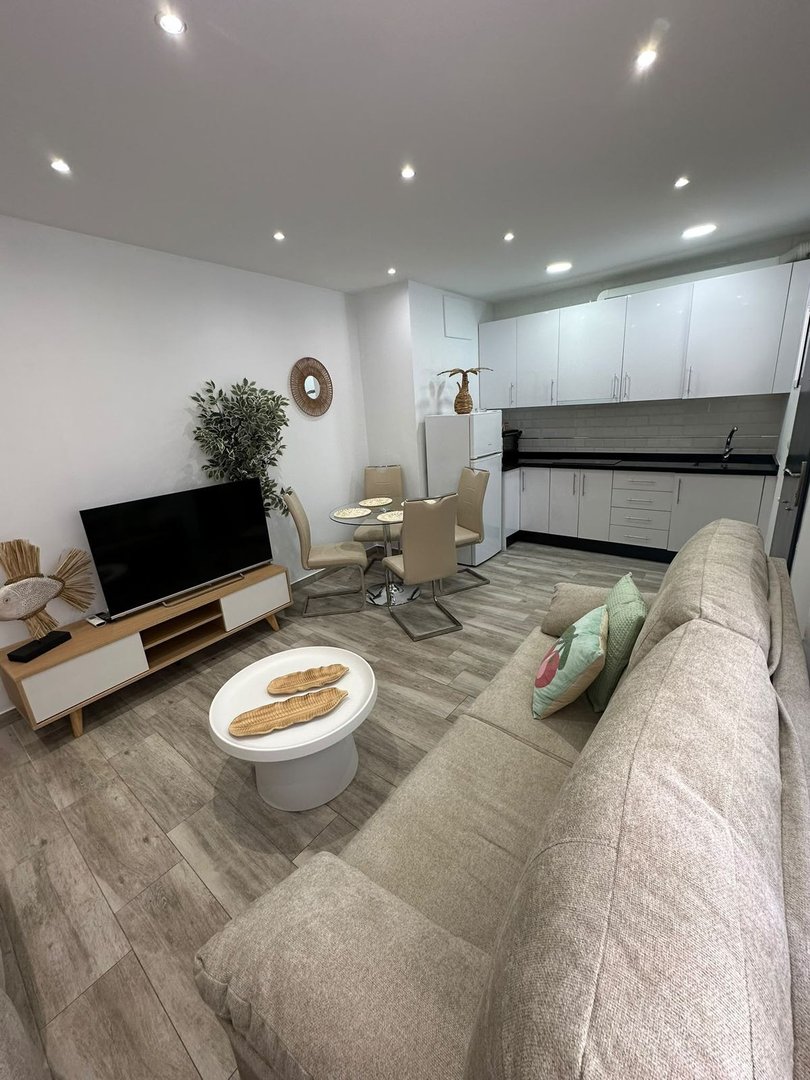 Modern living room with kitchenette, dining area, sofa, and TV. Bright and spacious interior design.