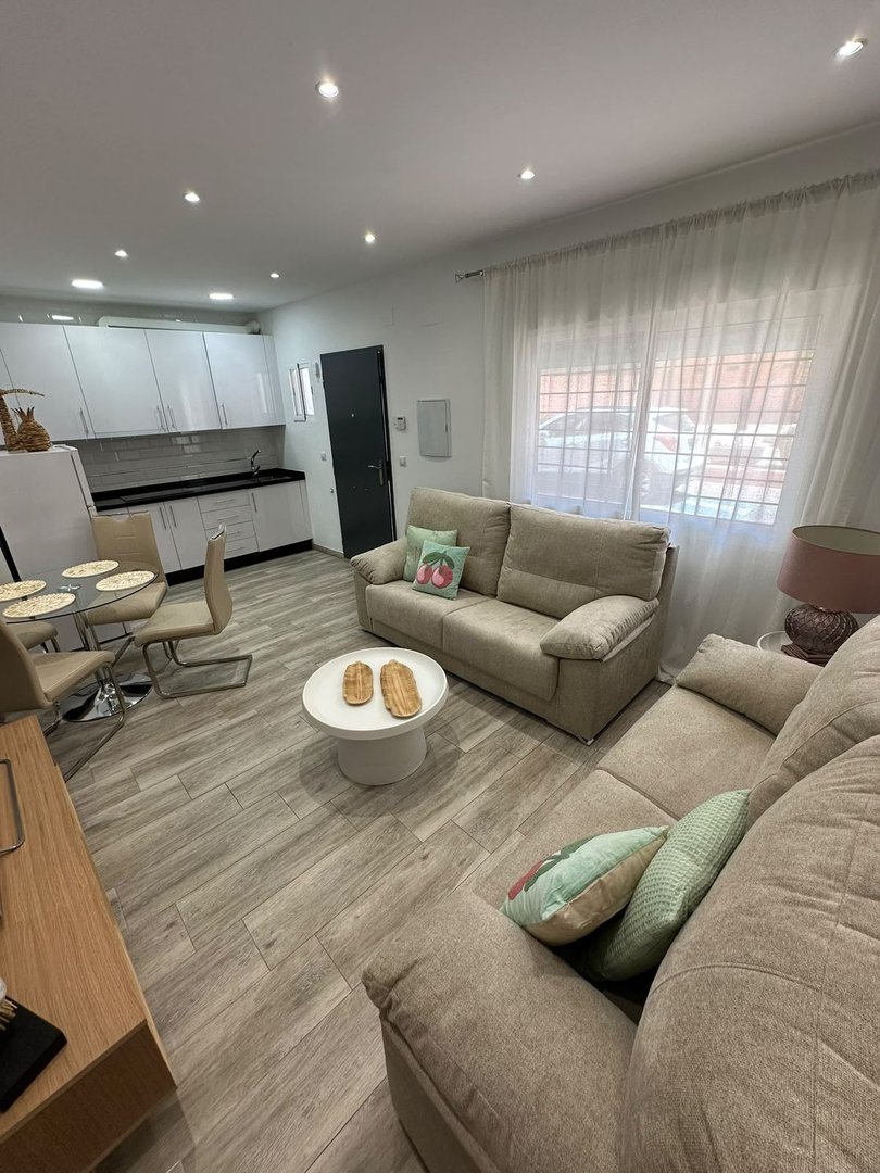 Modern living room with sectional sofa, dining area, and kitchenette. Bright space with large windows and comfortable seating.
