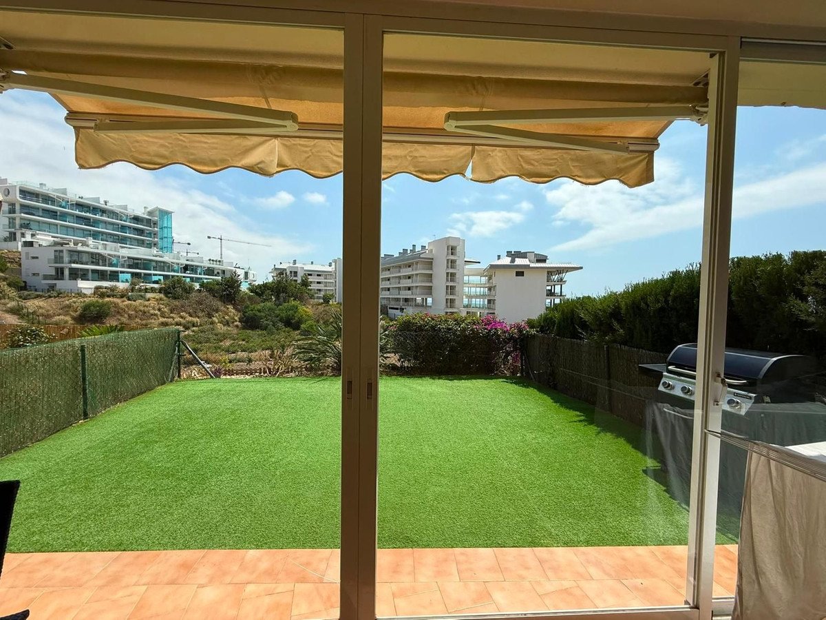 View from inside of a patio with a retractable awning, overlooking a green lawn and a barbecue grill.