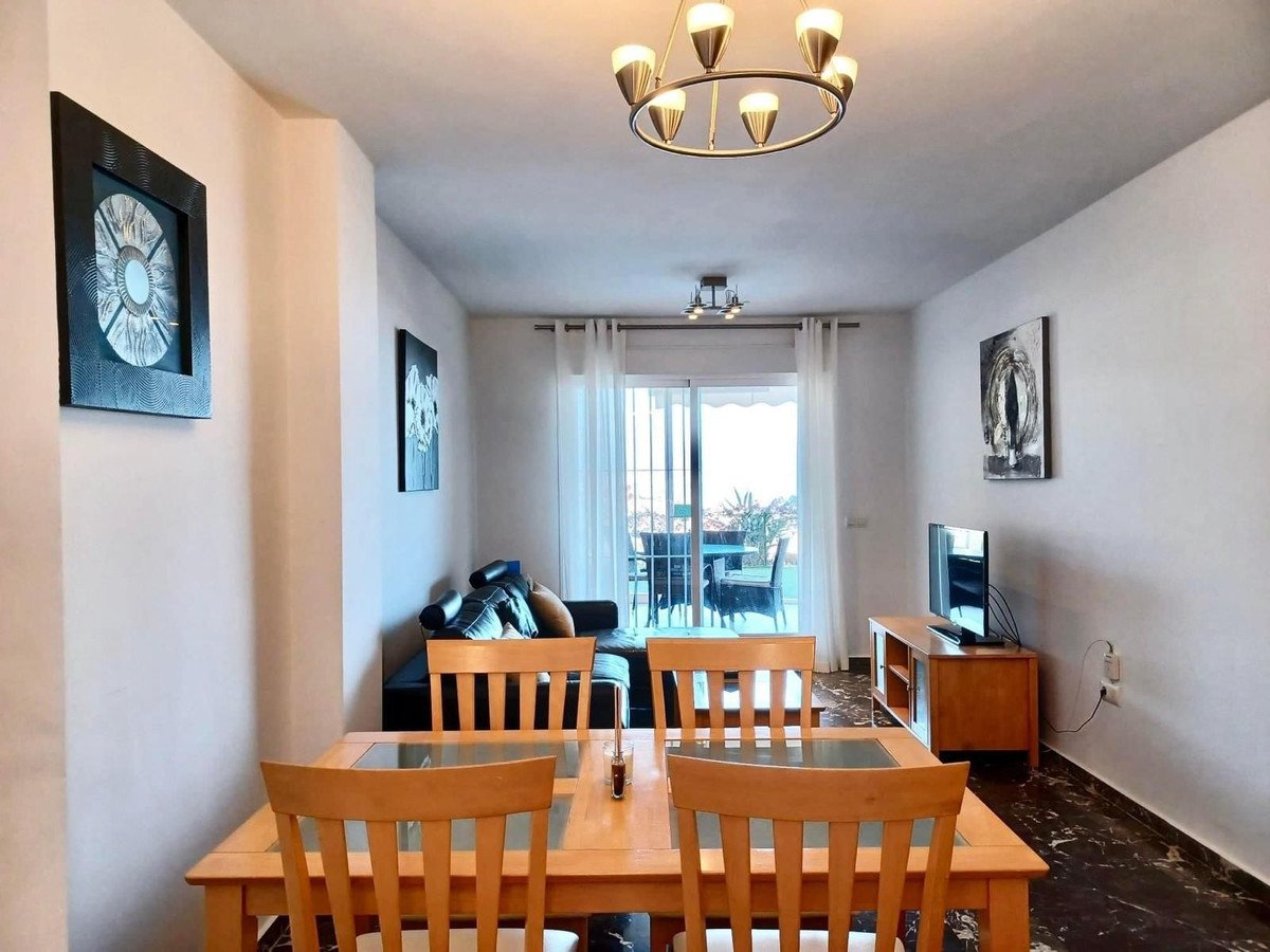 Cozy living and dining room with wooden furniture, sofa, TV, and a balcony with outdoor seating and a view.