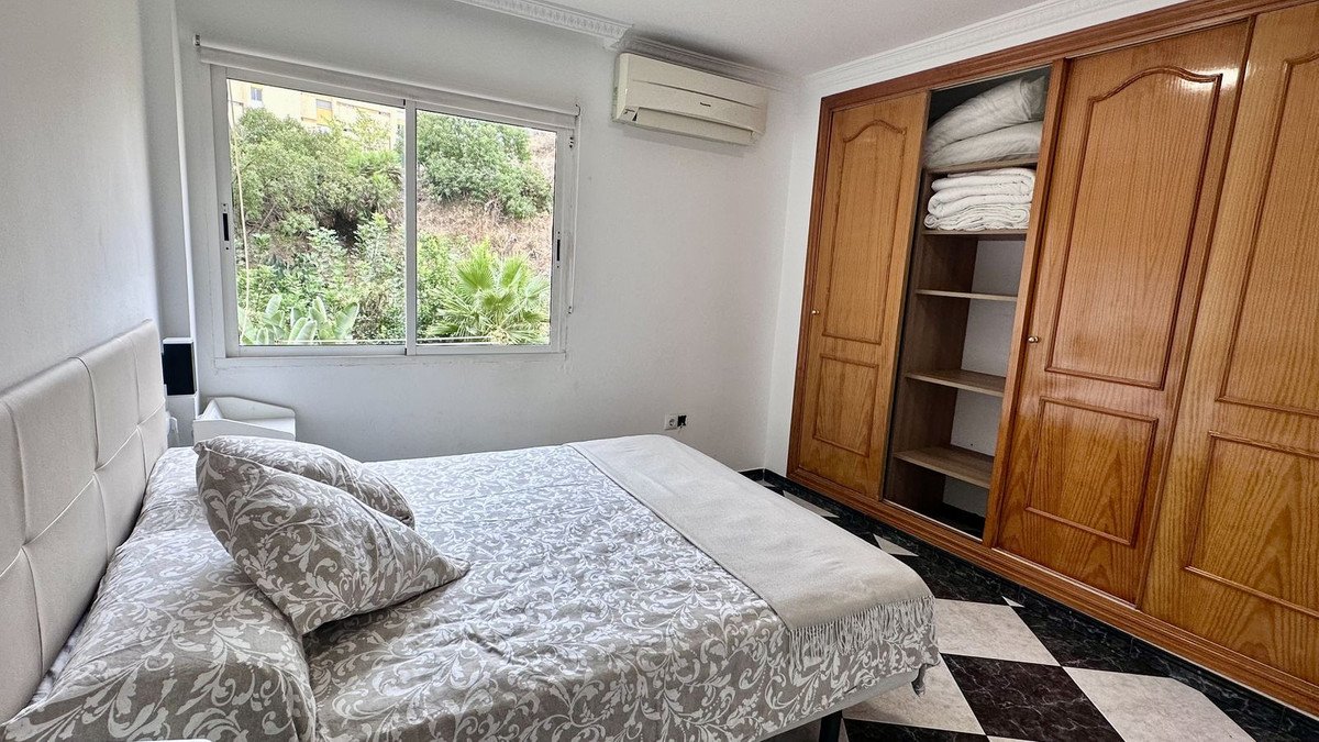 Bedroom with a large bed, garden view through the window, air conditioning, and a spacious wooden wardrobe.