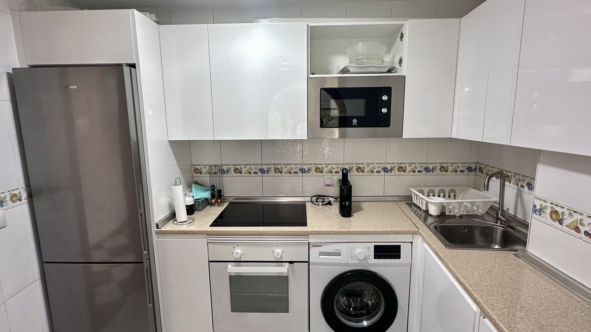 Modern kitchen with white cabinets, stainless steel refrigerator, microwave, oven, washing machine, and sink.
