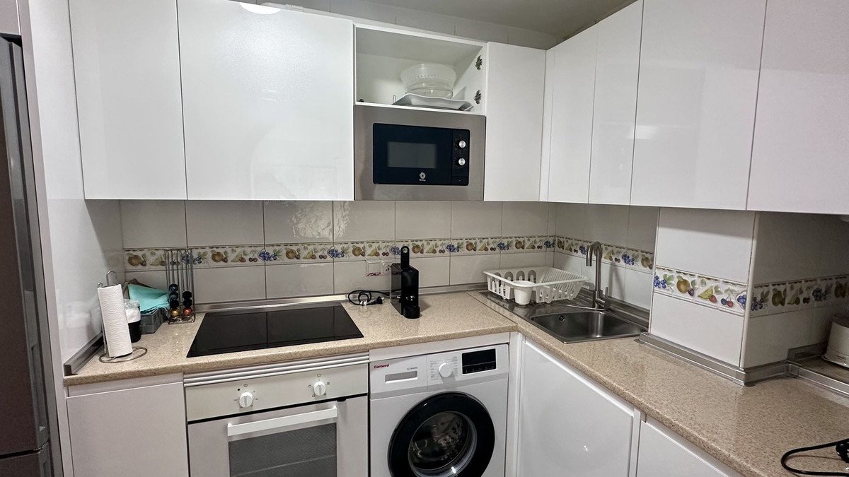 Modern white kitchen with induction hob, microwave, sink, and washing machine.