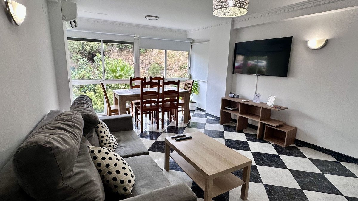 Comfortable living and dining area with a large sofa, wooden table, and chairs overlooking a lush green garden view.