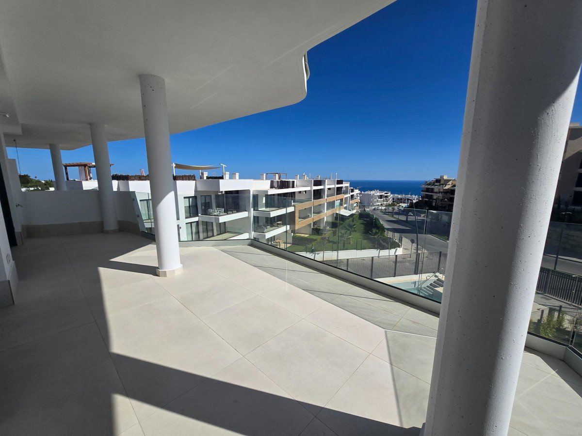 Spacious modern terrace with sea view overlooking buildings and the ocean under a clear blue sky.