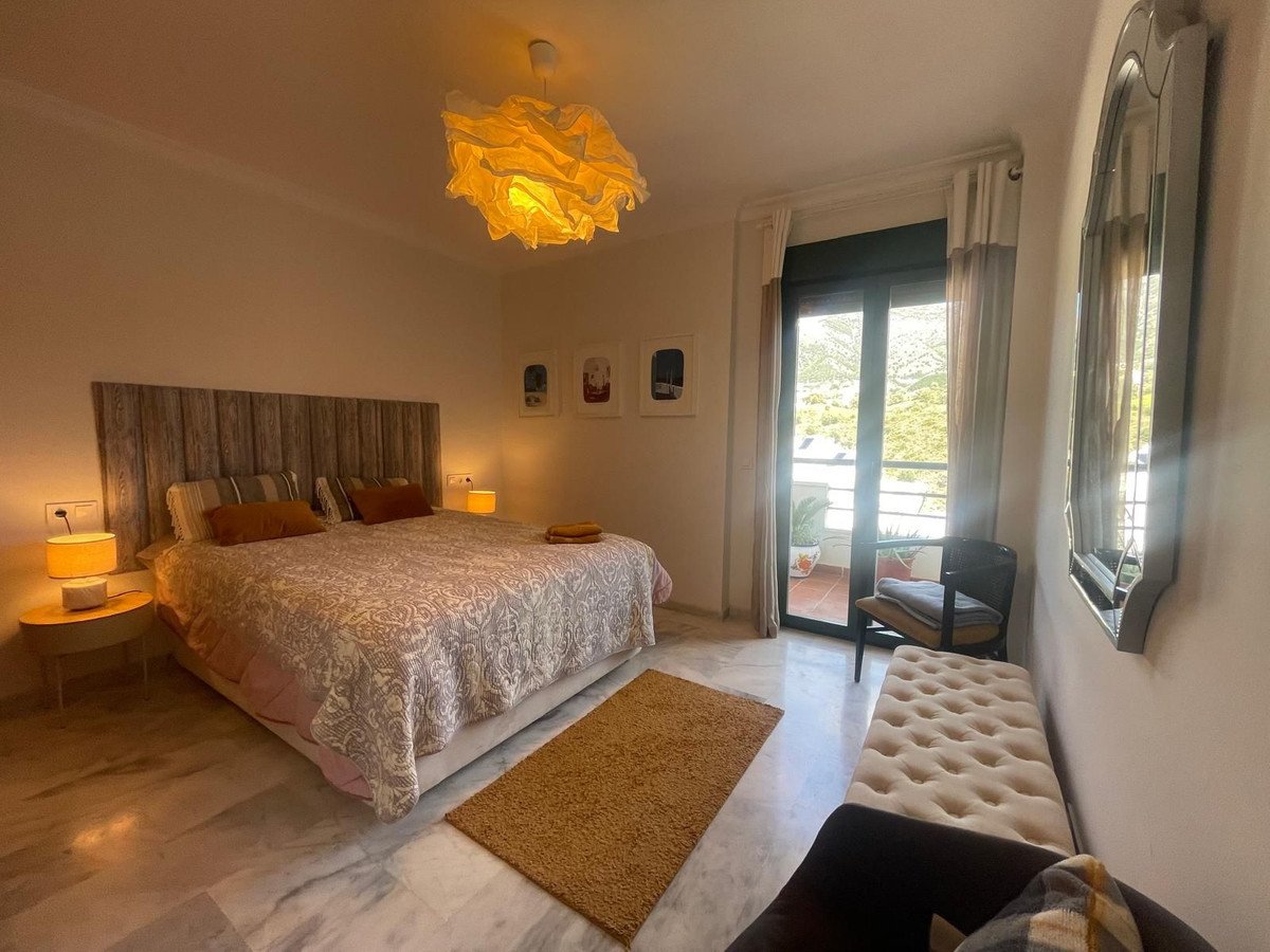 A bedroom with a king-size bed, decorative headboard, bedside lamps, and a balcony with a mountain view.