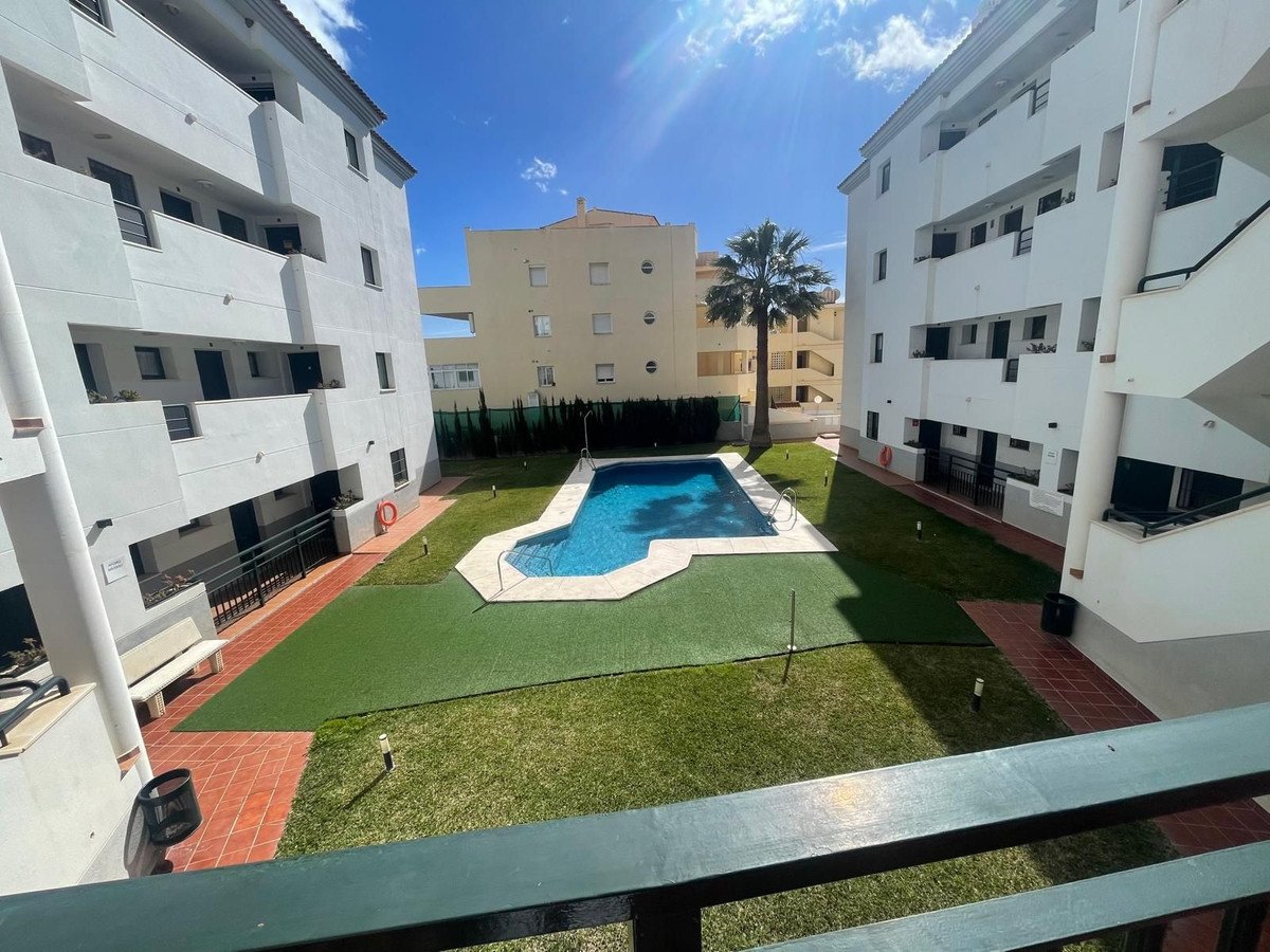 View of a communal courtyard with a swimming pool, surrounded by apartment buildings and a palm tree on a sunny day.