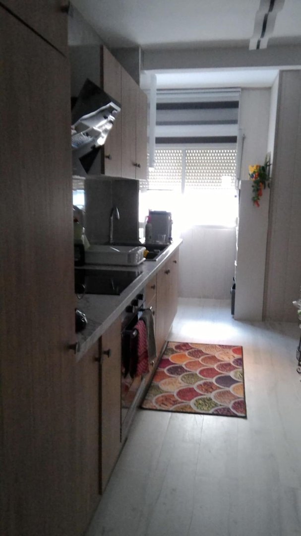 A modern kitchen with wooden cabinets, a countertop with appliances, and a window with blinds letting in natural light.