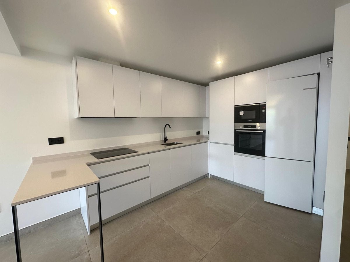 A modern white kitchen with sleek cabinets, integrated oven and microwave, and a breakfast bar. Features built-in appliances.