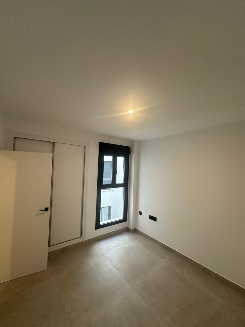 Modern empty bedroom with tiled floor, large window, and a white sliding door closet.