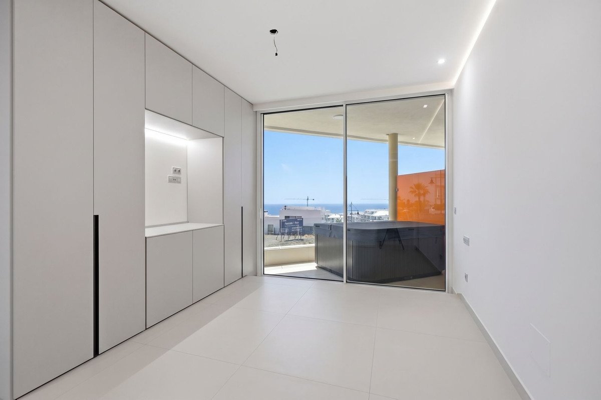 Modern room with built-in closets, sliding glass doors opening to a balcony with a hot tub and a view of the sea and sky.