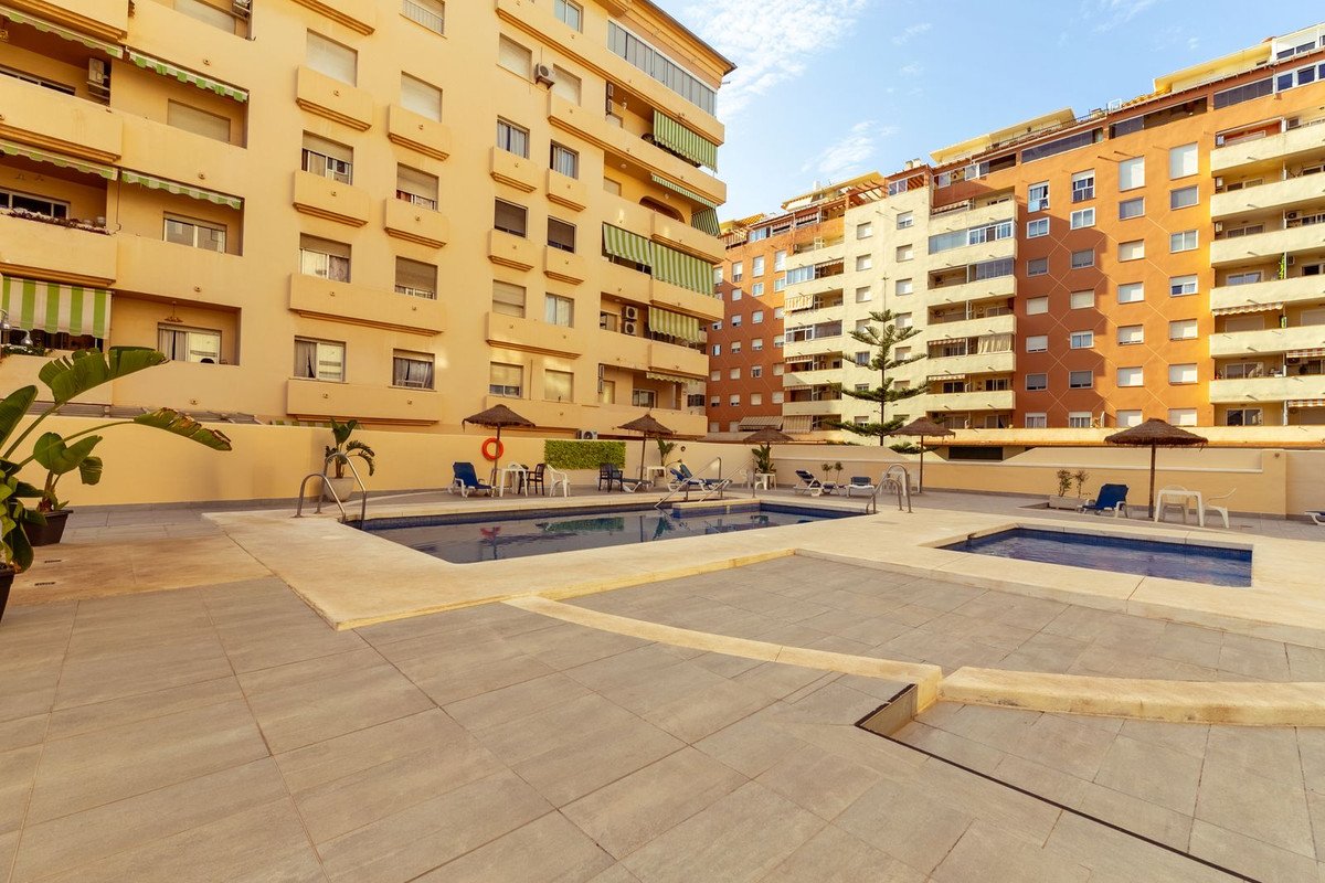 Communal swimming pools and lounge chairs in front of apartment buildings under a blue sky.