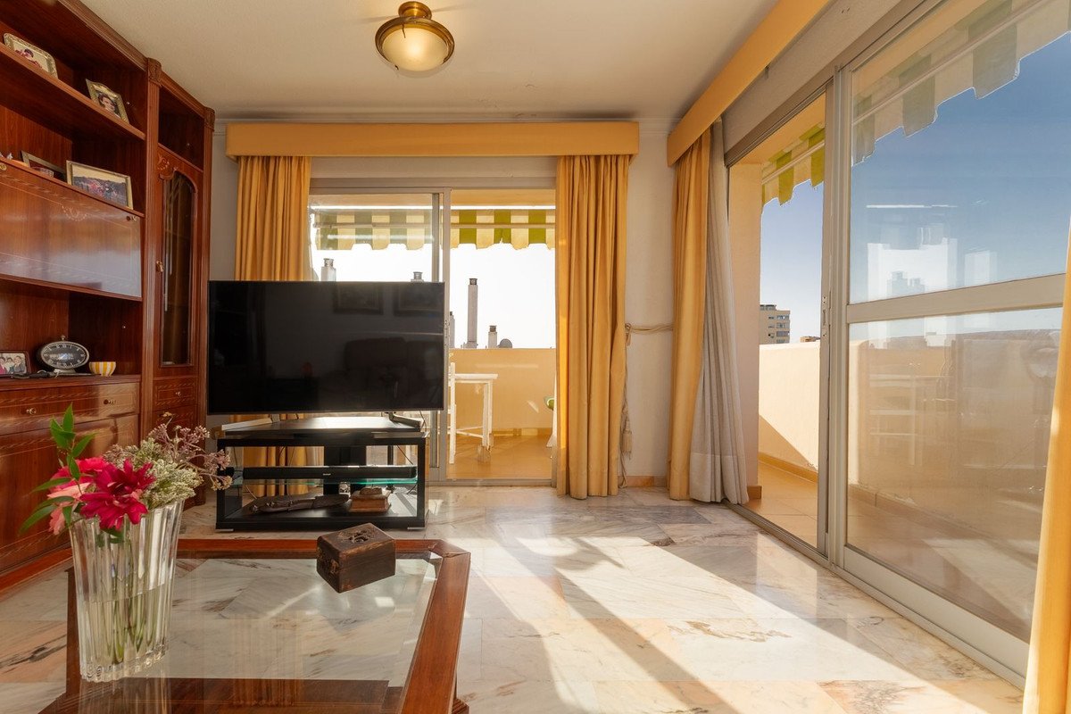Living room with large TV, wooden bookshelf, marble floor, and balcony access with a sunny outdoor view.