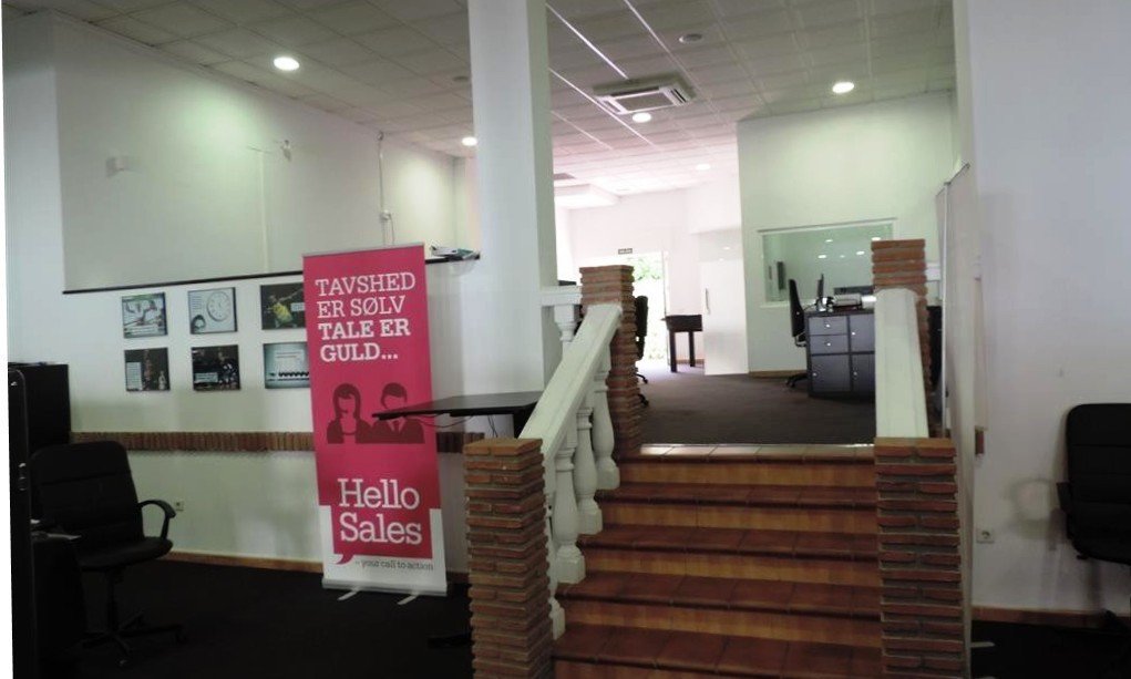 Interior office view with a 'Hello Sales' banner, framed pictures on the wall, and stairs leading up.
