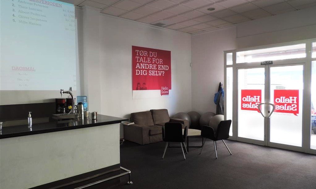 Reception area with a bar, lounge seating, and a glass entrance with 'Hello Sales' signs.