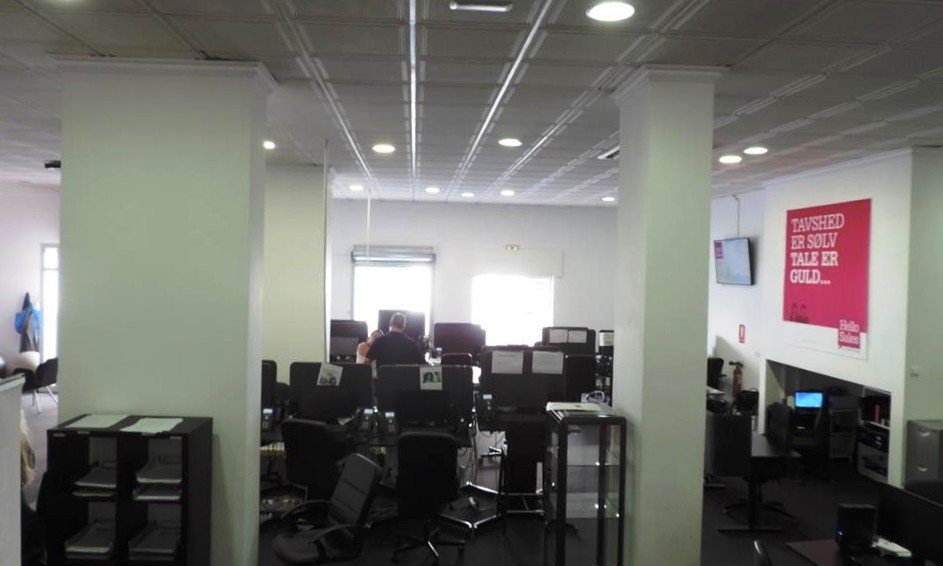 Modern office interior with multiple computer workstations, desks, and chairs. Large motivational poster on the wall.