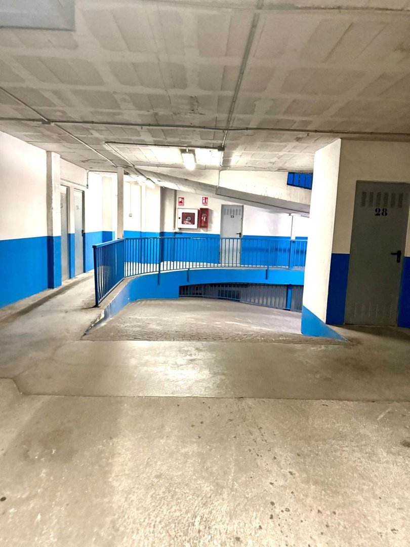 Concrete parking garage with blue painted walls, metal railing, and a ramp leading down.