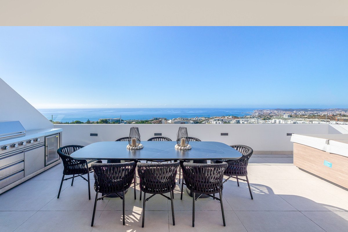 Outdoor dining table with chairs, grill, and hot tub on a terrace with a panoramic sea and city view.