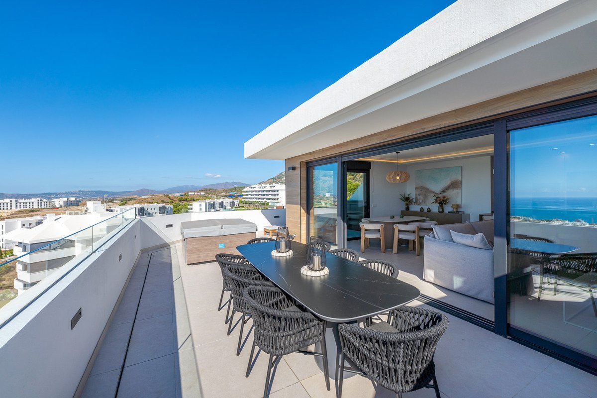 Spacious terrace with outdoor dining set and hot tub, overlooking the sea and a modern residential area.