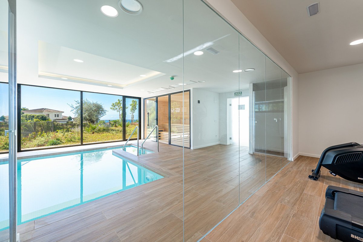 Indoor swimming pool and sauna with ocean views, adjacent to a gym with treadmills.