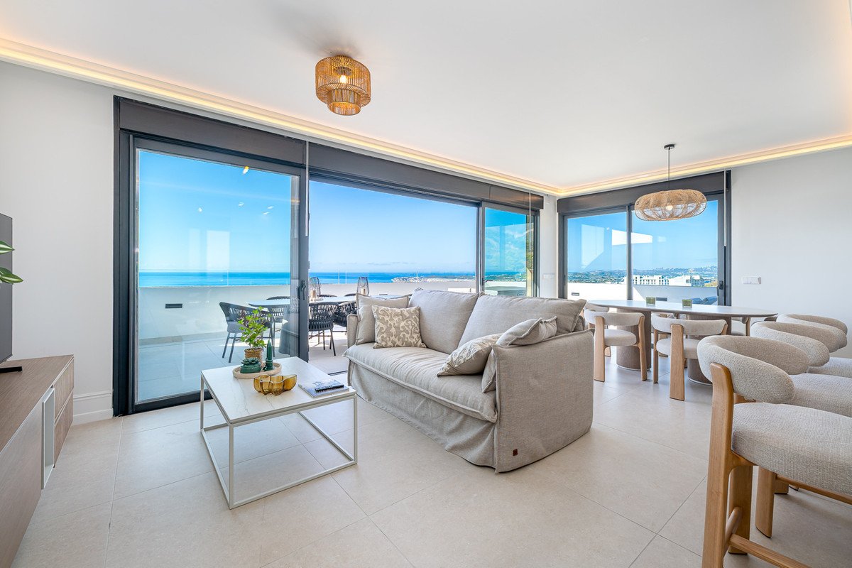 Spacious living and dining area with comfortable seating, large windows, and a balcony with a sea view.
