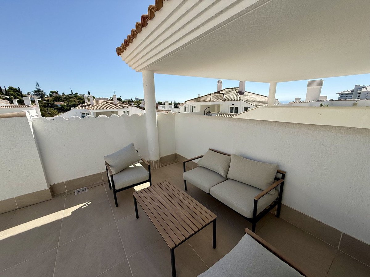 A furnished terrace with a sofa, chairs, and coffee table, offering a view of rooftops and distant sea.