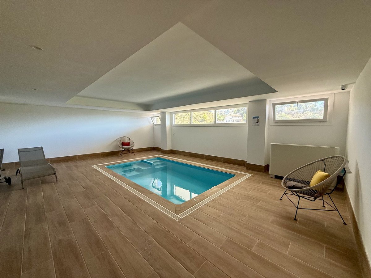 Indoor swimming pool area with lounge chairs and modern seating, featuring natural light from windows.