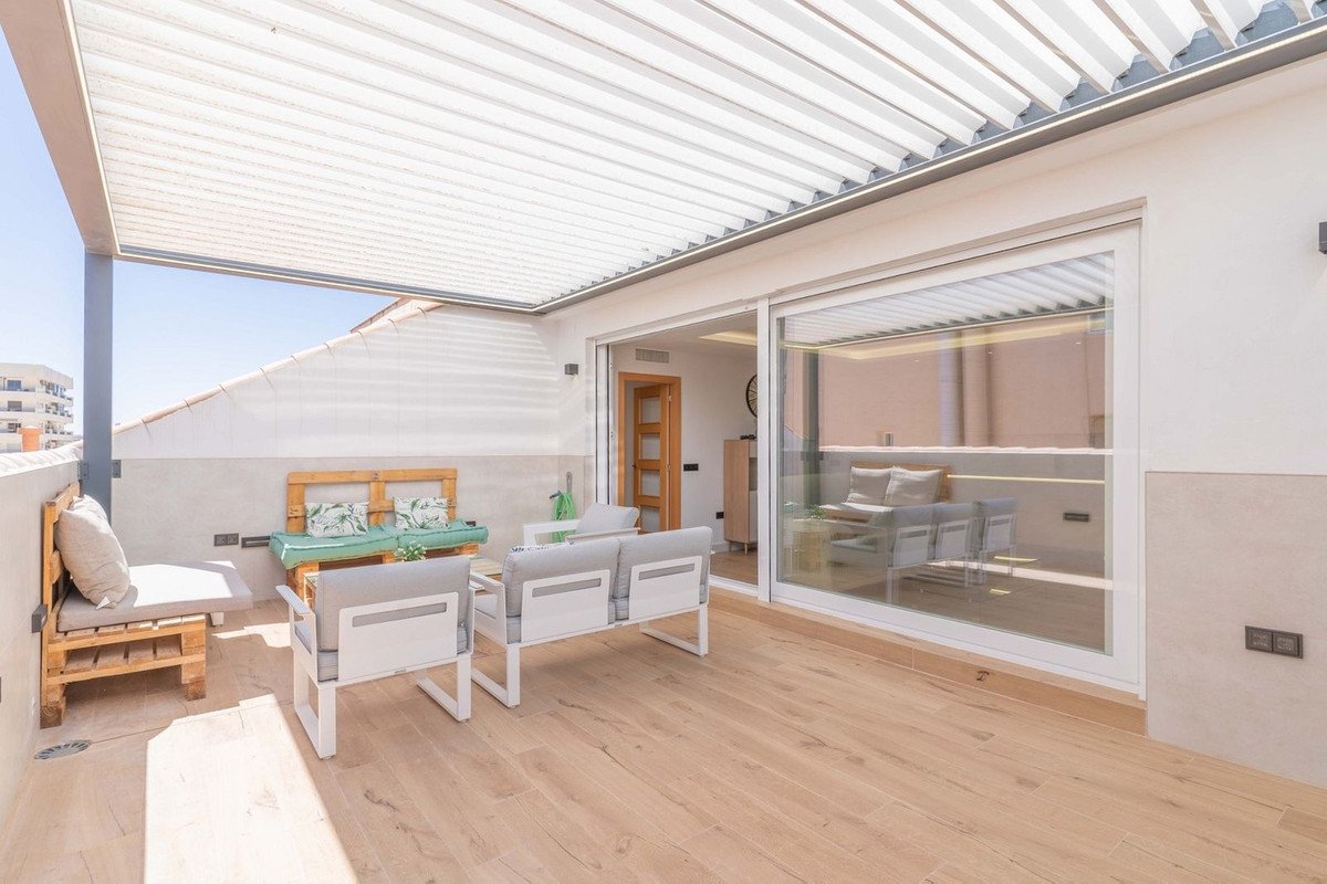 Modern terrace with outdoor seating, sofa, and coffee table under a retractable awning, overlooking urban landscape.