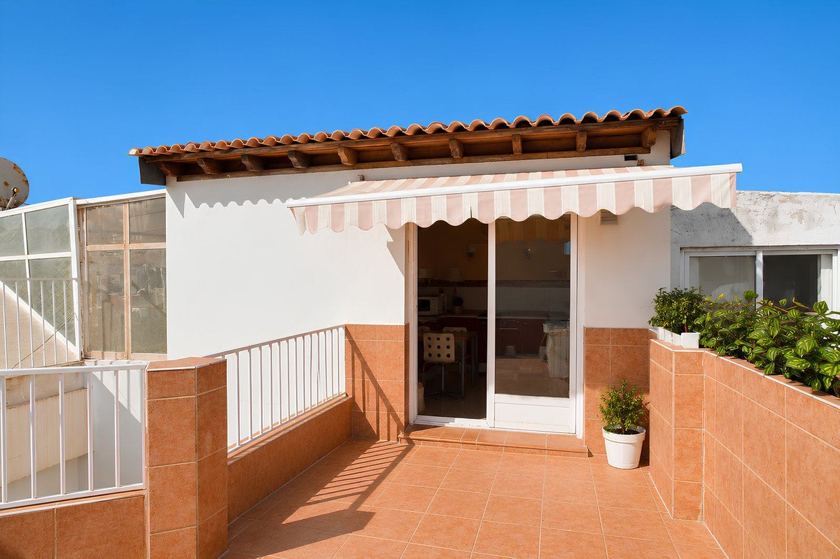 Rooftop terrace with tiled floor, white railing, and striped awning over glass door entrance.