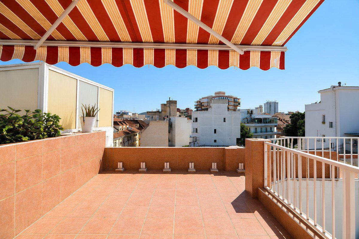 Rooftop terrace with red and white awning, tiled floor, and city view.
