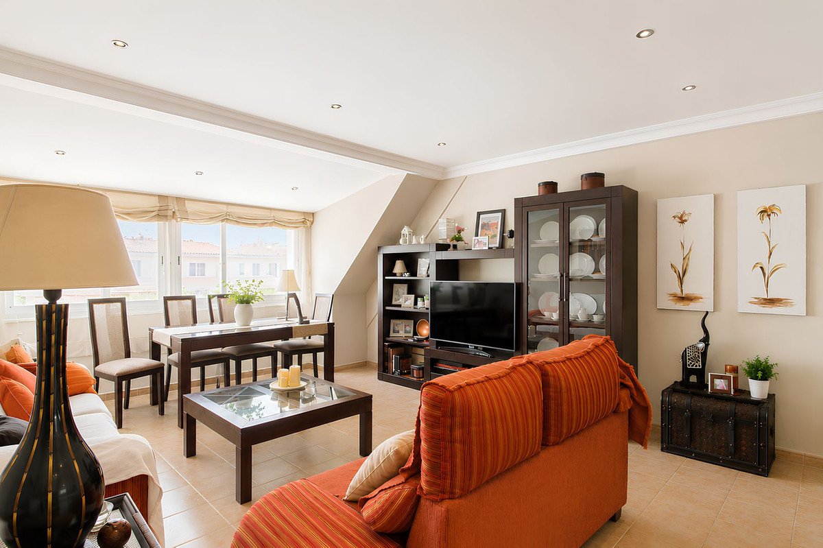 Spacious living room with orange sofa, dining table, TV unit, and large windows offering a city view.
