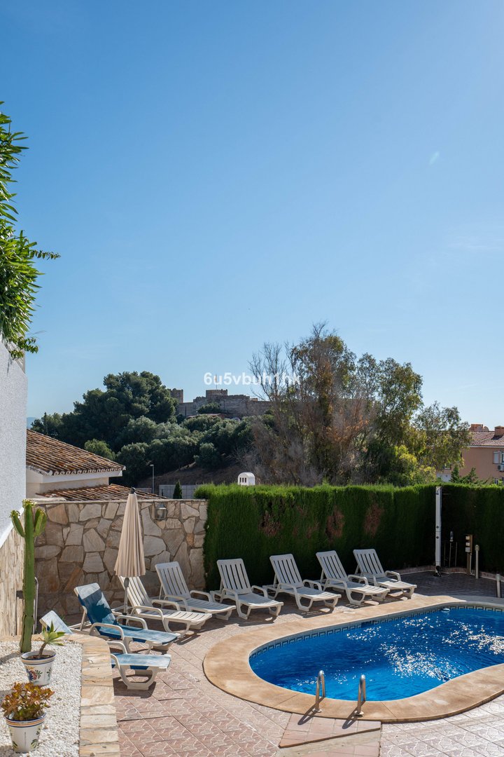 Outdoor swimming pool with sun loungers on a terrace, overlooking a castle on a hill under a clear blue sky.
