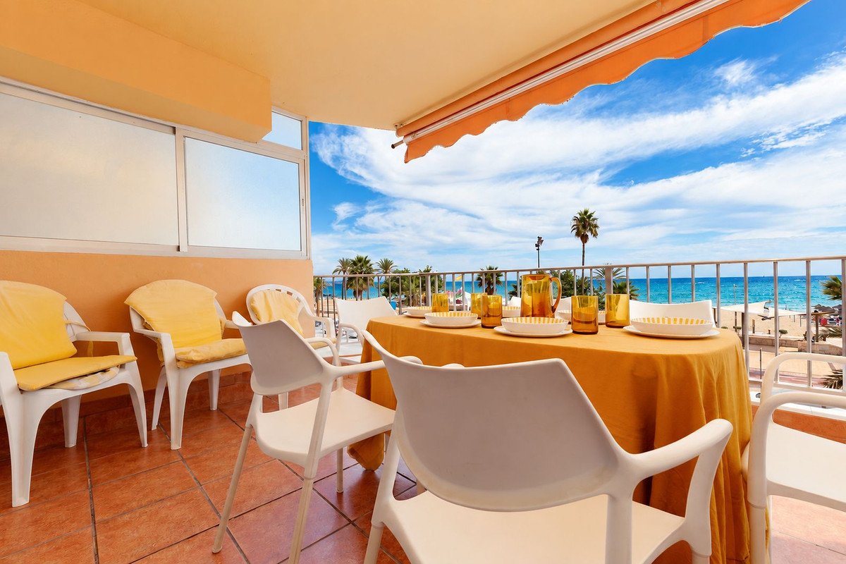 Outdoor dining area on a balcony with a sea view, set table with yellow tablecloth and chairs.