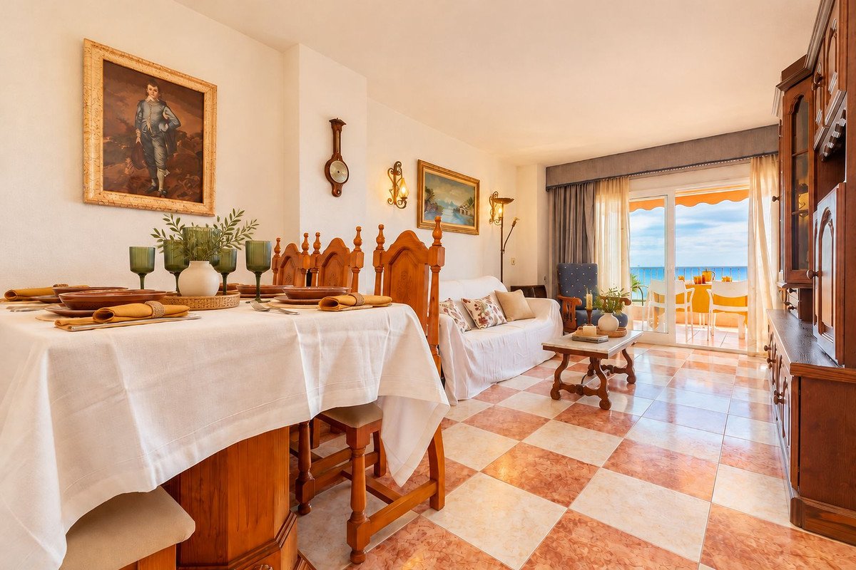 A dining and living area with a table set for dinner and a sofa, leading to a balcony with a sea view.