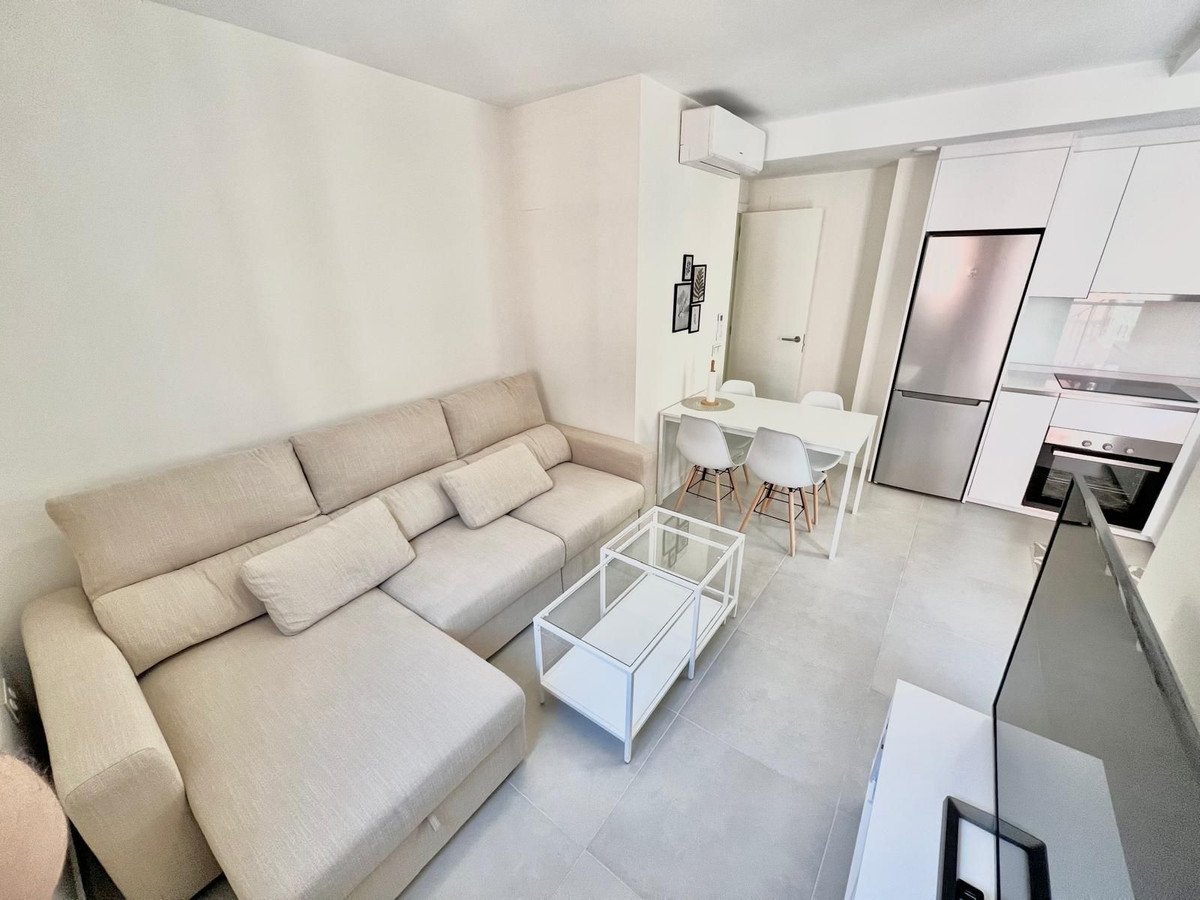 Modern open-plan living and dining area with beige sofa, glass coffee table, and kitchen.