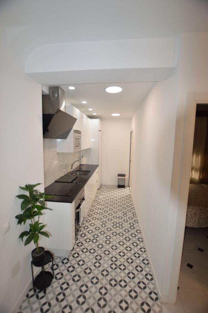 Modern galley kitchen with black and white tile floor, white cabinets, and stainless steel range hood.