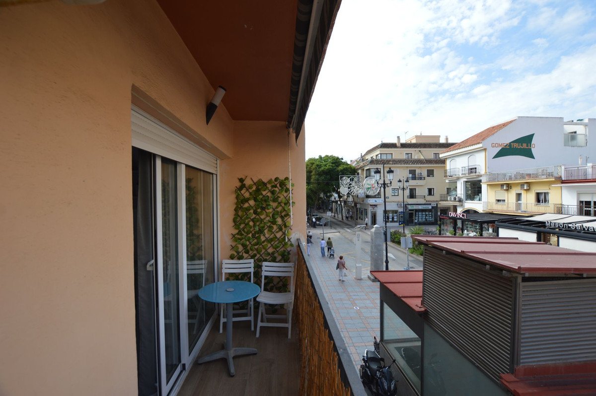 Apartment balcony with table and chairs overlooking a street with buildings and pedestrians