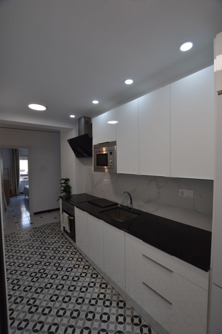 Modern kitchen with black countertops, white cabinets, and patterned tile floor.