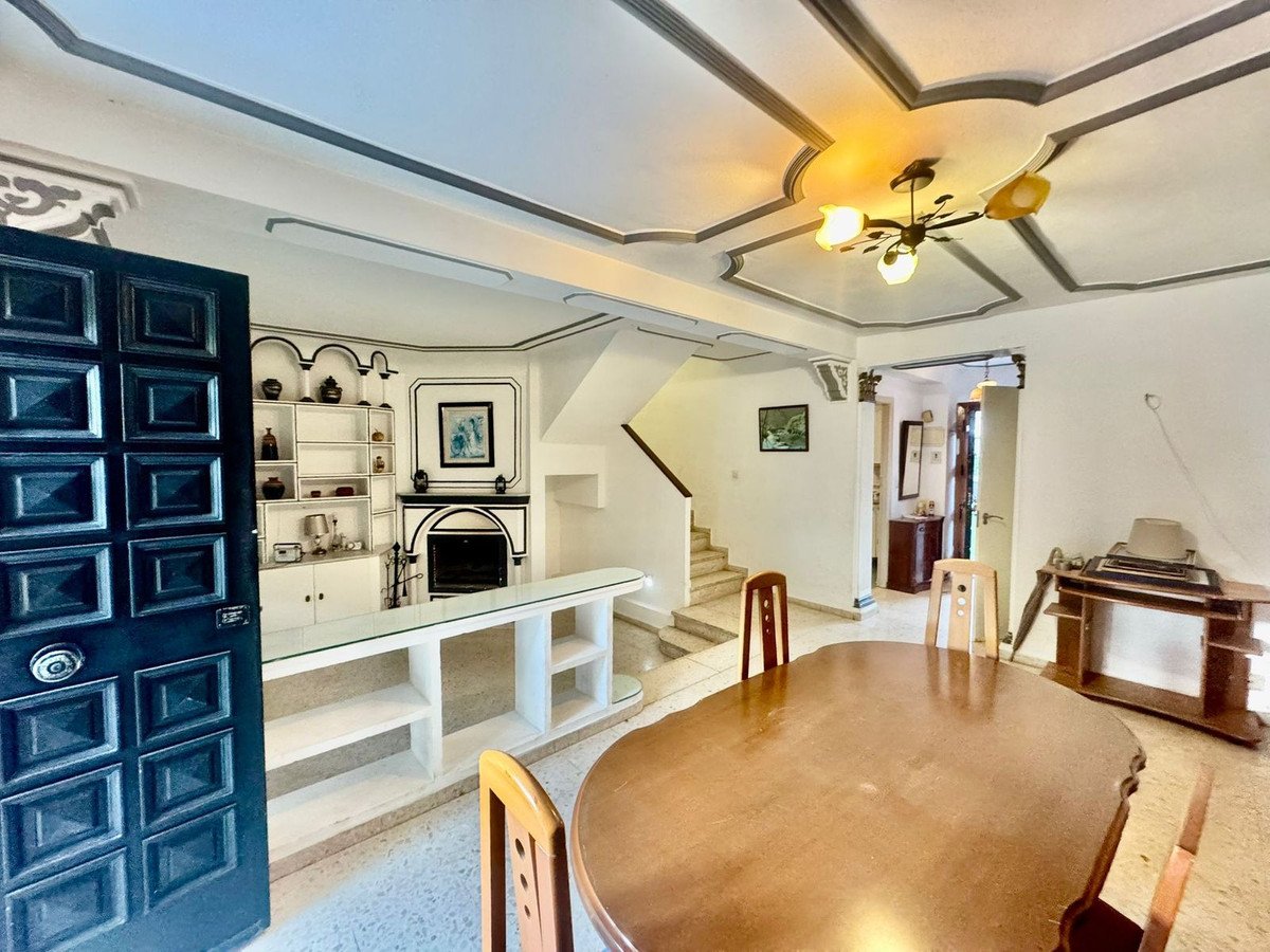 Interior view of a living and dining room with a fireplace, staircase, and large wooden table.