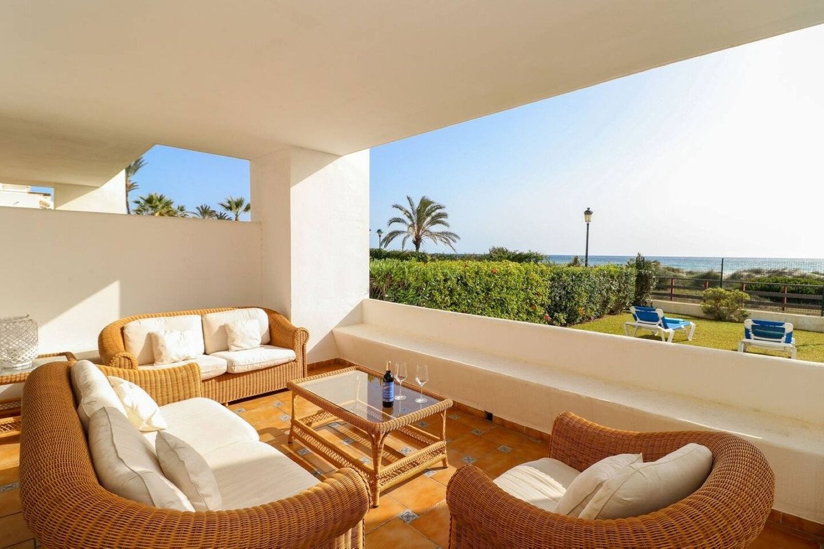 Spacious terrace with rattan lounge furniture, offering a beautiful sea view with palm trees and loungers on the lawn.