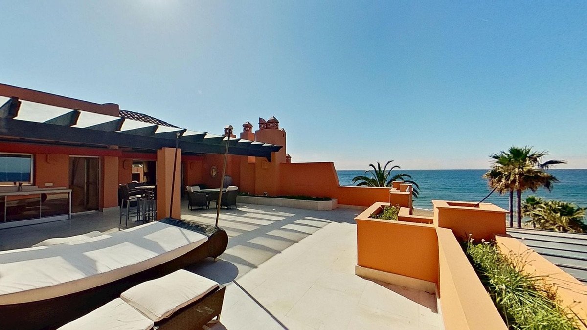 Spacious terrace with lounge chairs and dining area, offering a stunning sea view with palm trees.
