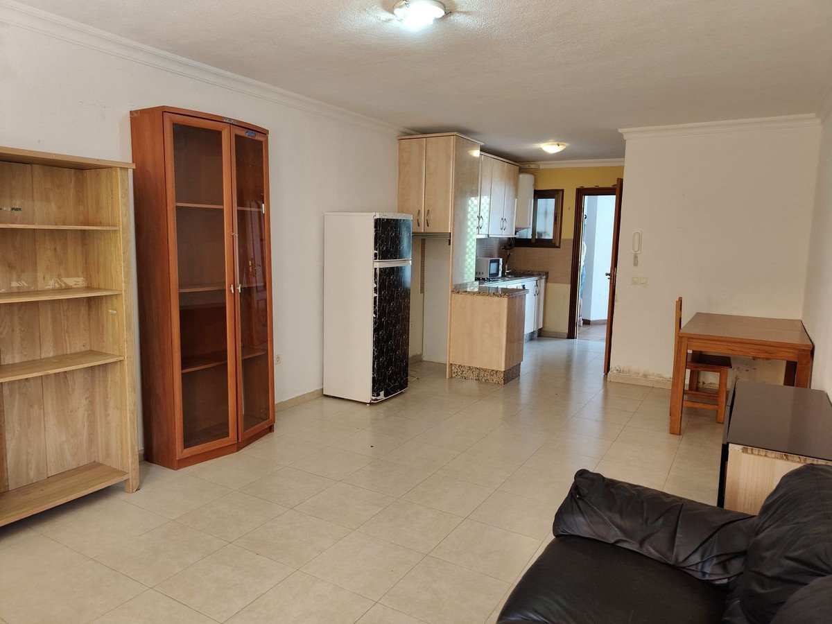 Living area with kitchen and dining space, featuring cabinets, a refrigerator, shelves, and a sofa.