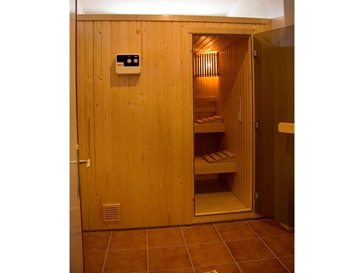 Wooden sauna with benches, control panel, and warm lighting.