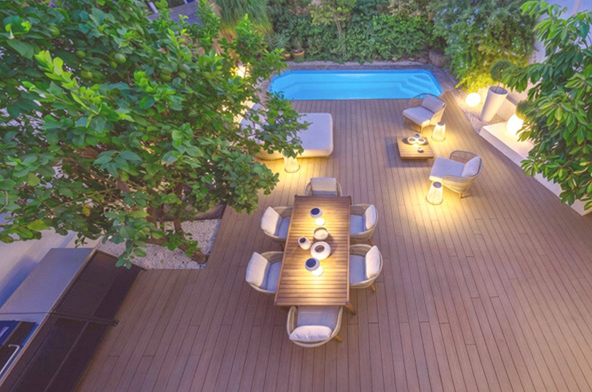 Outdoor patio with a dining table, lounge seating, and a swimming pool, illuminated by modern lighting.