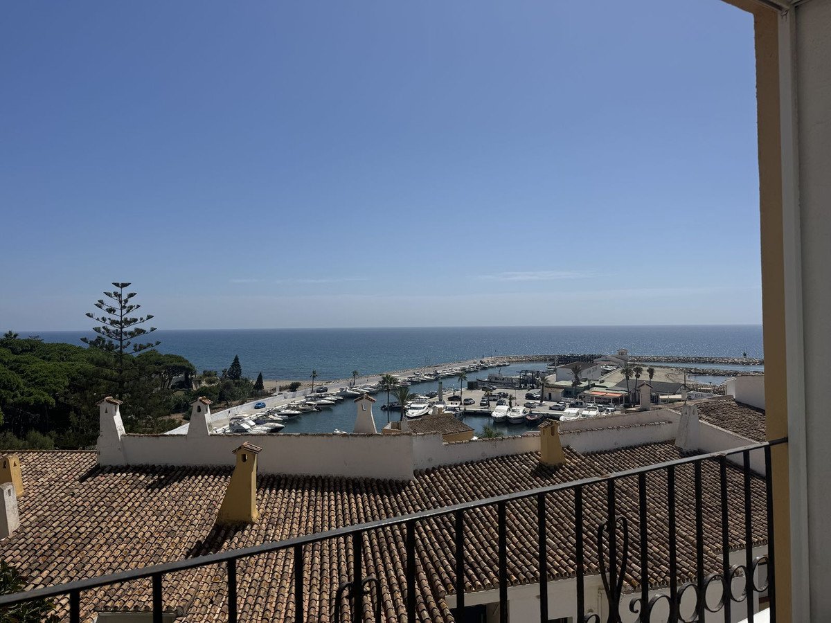 Balcony view of a marina with boats, sea, and tiled rooftops under a clear blue sky.