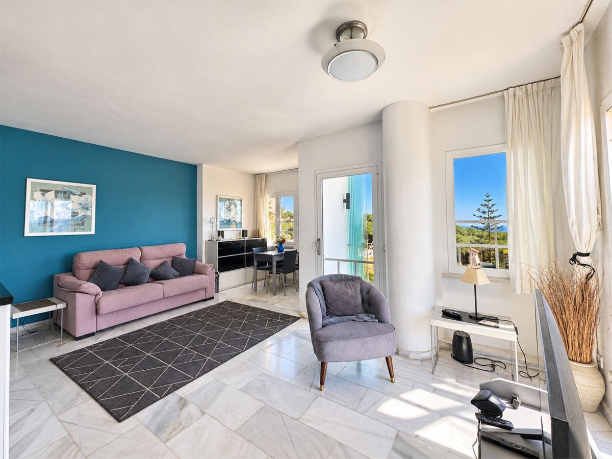 Living room with a pink sofa, blue accent wall, armchair, and a window with a sea view.