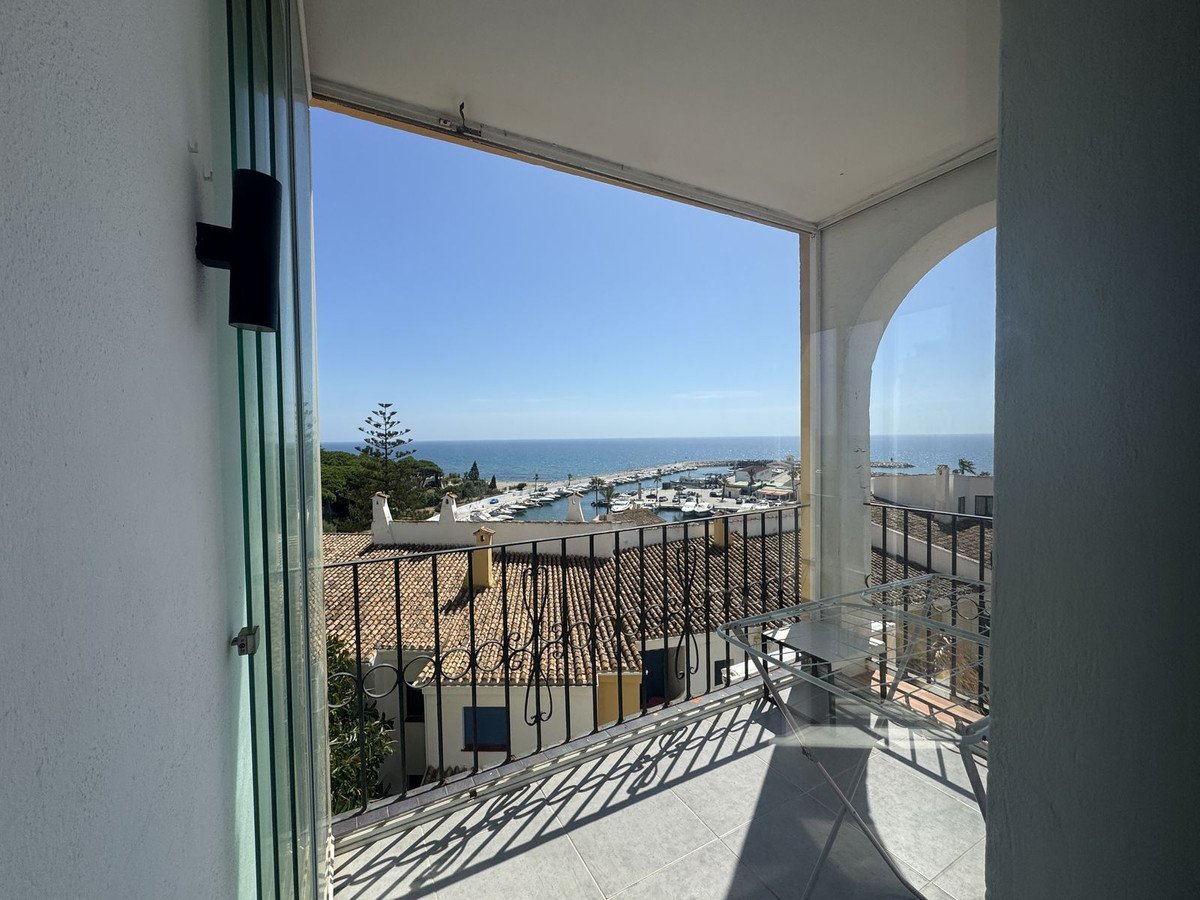Balcony with a view of a marina and the sea, overlooking rooftops and buildings under a clear blue sky.