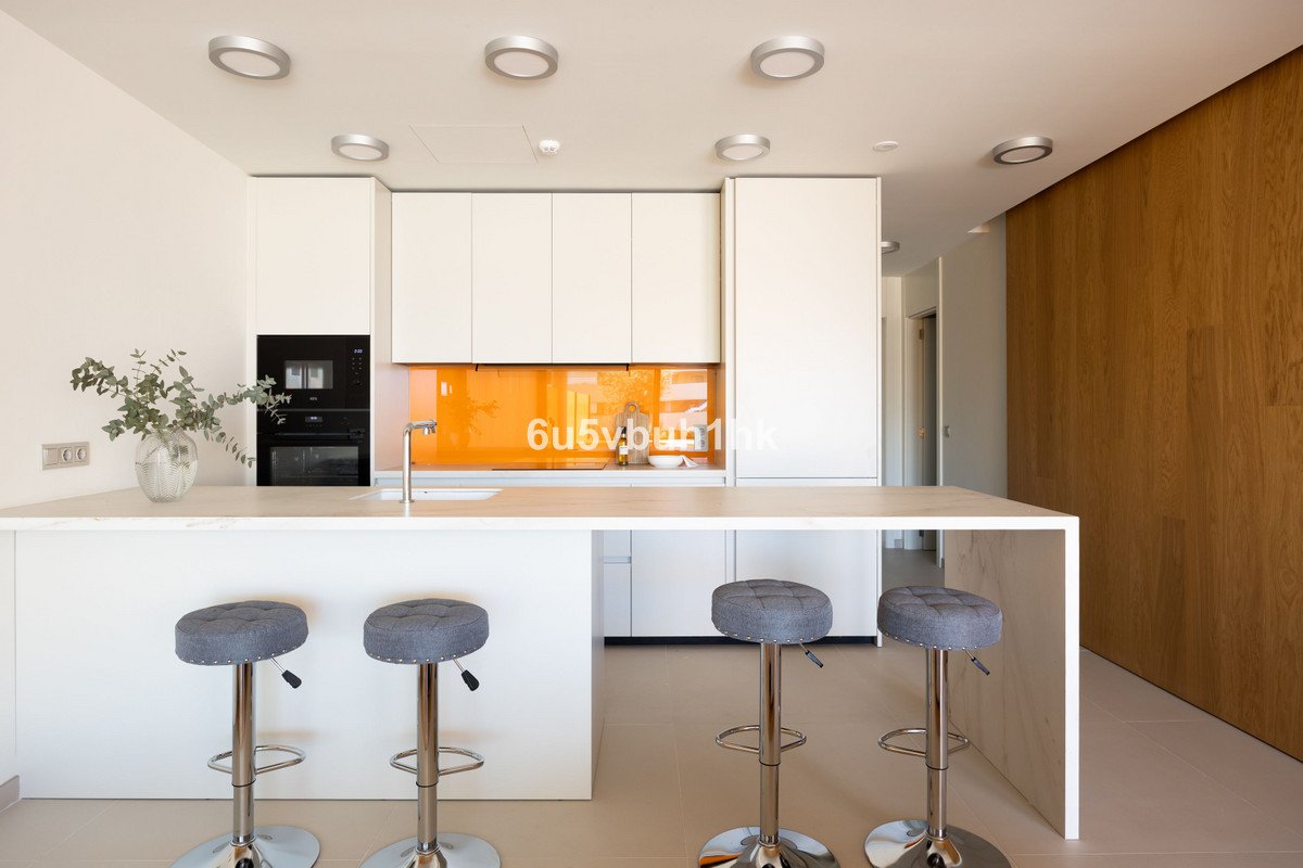 Modern kitchen with white cabinets, an orange backsplash, a breakfast bar with stools, and a built-in oven.