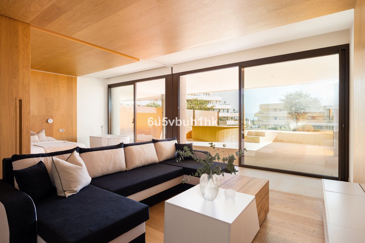 Modern living area with sectional sofa, king bed, and large windows leading to an outdoor terrace with buildings and trees in the distance.